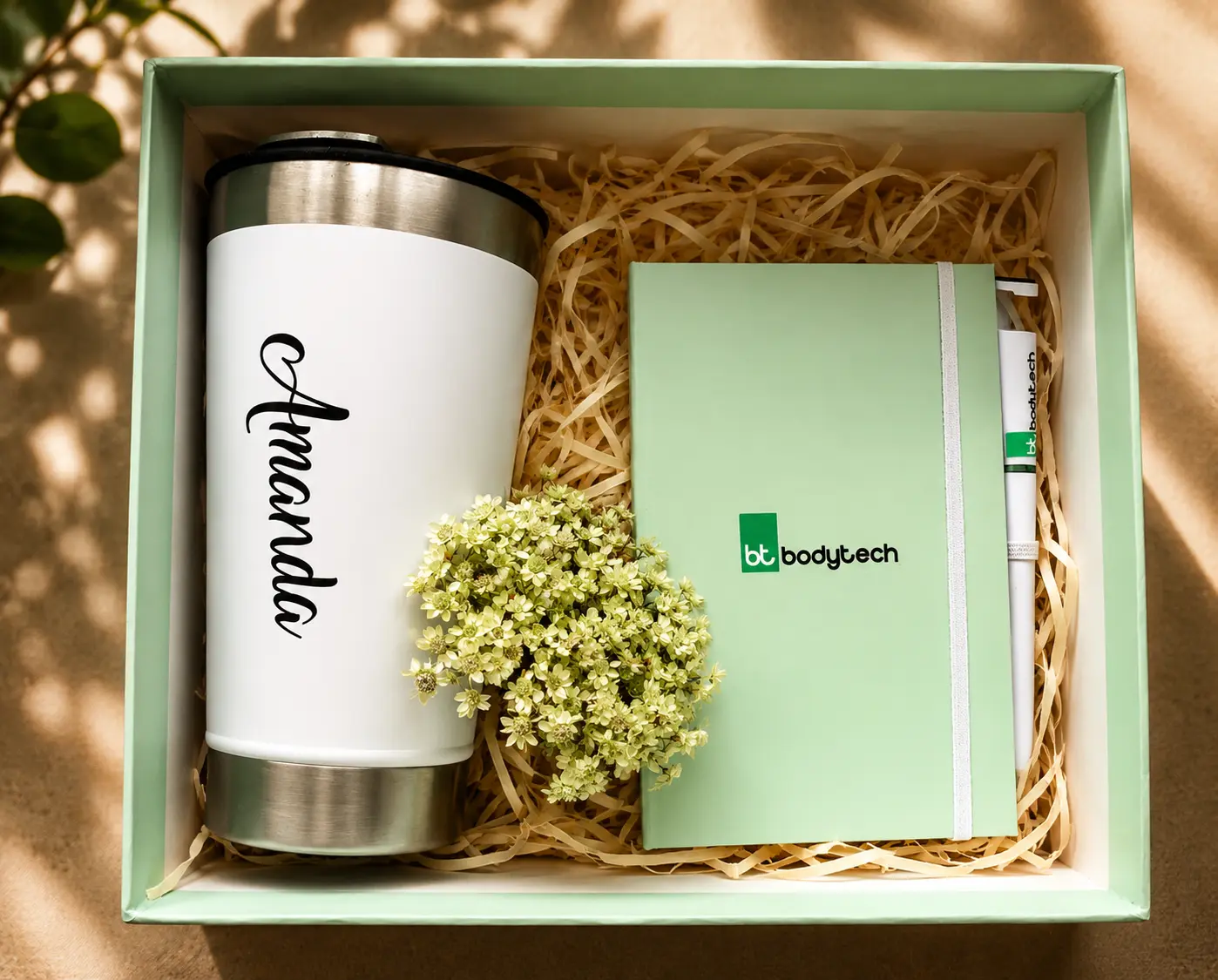 Caixa verde-clara aberta com copo térmico com nome, caderno e caneta personalizados